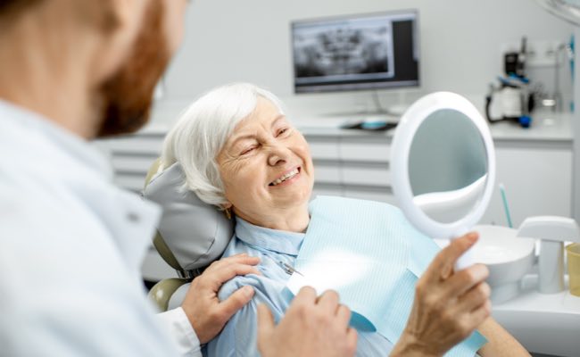 Woman at the dentist looking at herself in a mirror smiling.