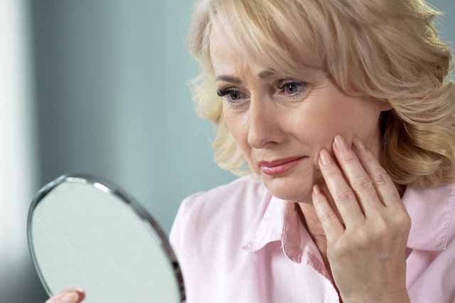 Woman looking at herself in the mirror, holding her hand on her cheek.